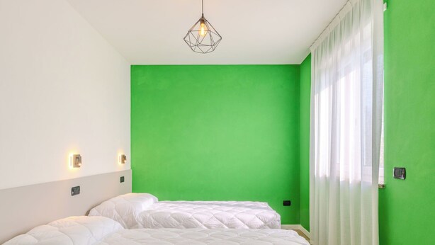 A room with two beds, a green wall, a hanging light fixture, and a window with sheer curtains. - Garda Oasis and Horizon by Interhome (Riva del Garda)