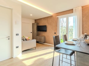 A modern dining area with a table set for two, a sofa, and a TV mounted on the wall. - Garda Oasis and Horizon by Interhome (Riva del Garda)