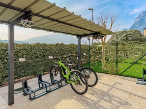 A covered bike parking area with two bicycles, a bike rack, and a view of a mountainous landscape. - Garda Oasis and Horizon by Interhome (Riva del Garda)