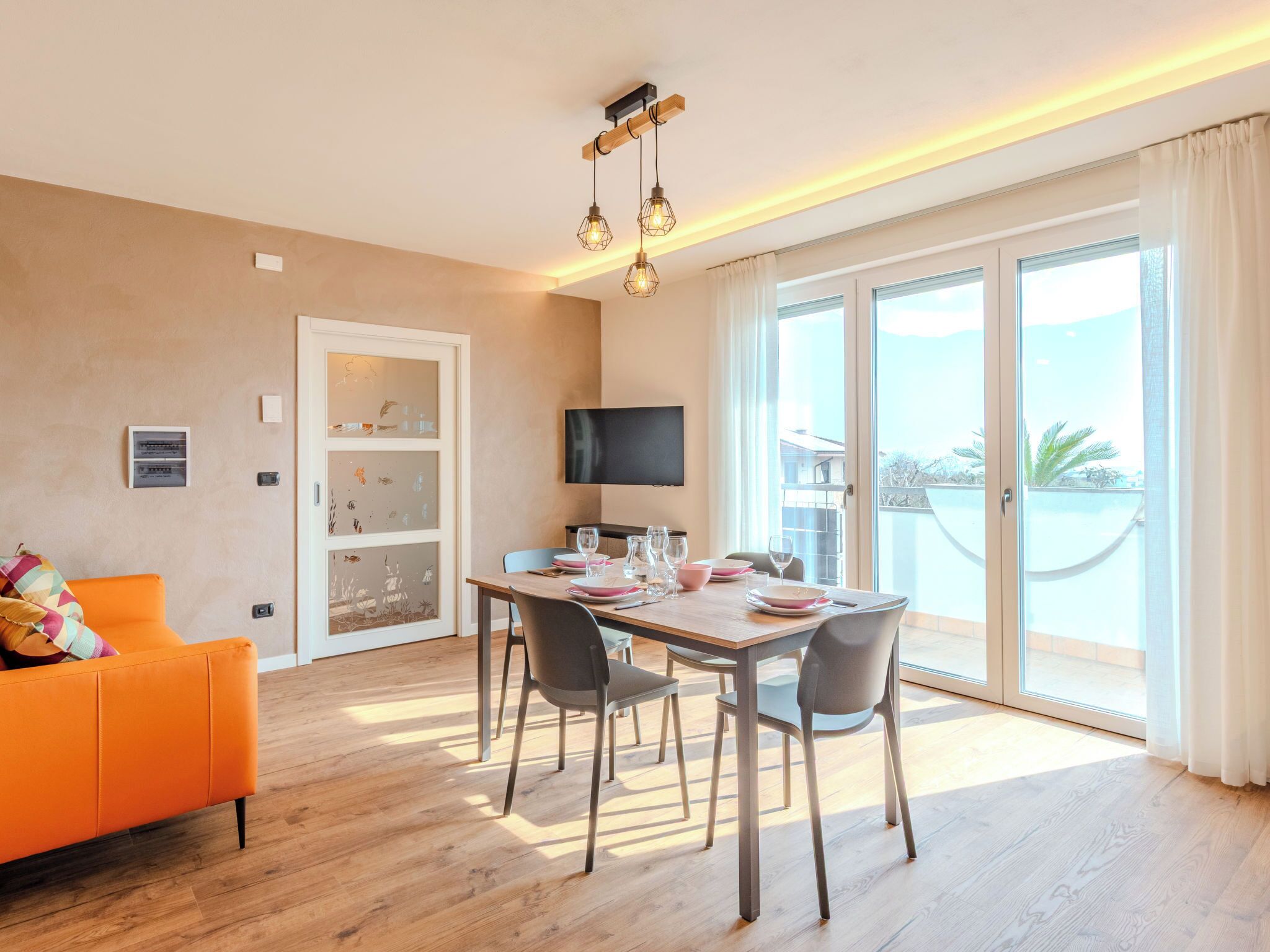 A modern living room with a dining area, a sofa, a TV, and a balcony with a view.
