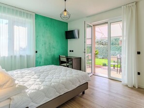 Ein Schlafzimmer mit einem Bett, einem Schreibtisch, einem Fernseher und einer Glastür, die zu einem Außenbereich führt.