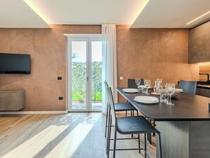 Eine moderne Küche mit Essbereich, einem an der Wand montierten Fernseher und einer Glastür, die in einen Garten führt.