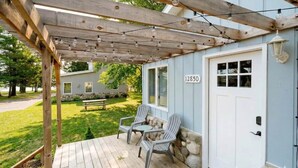 A wooden deck with two Adirondack chairs, a white door with a mailbox, and a stone wall.