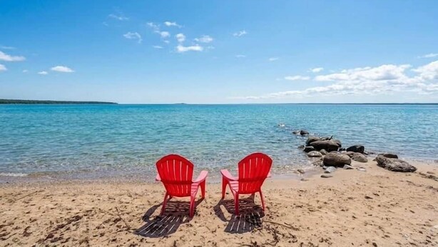 A beach with two red chairs facing the sea, clear blue sky, and calm water.