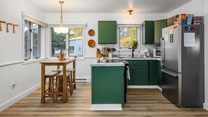 A modern kitchen with green cabinets, a stainless steel refrigerator, and a wooden dining table with benches.