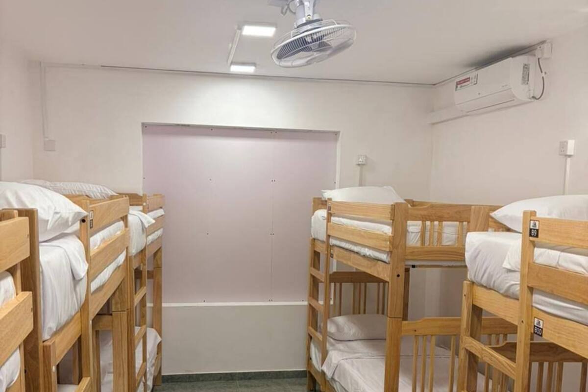 Una stanza con letti a castello, una ventola a soffitto, un condizionatore d'aria e una parete semplice.