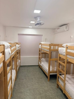 Huoneessa on kerrossängyt, kattotuuletin, ilmastointilaite ja pelkistetty seinä.