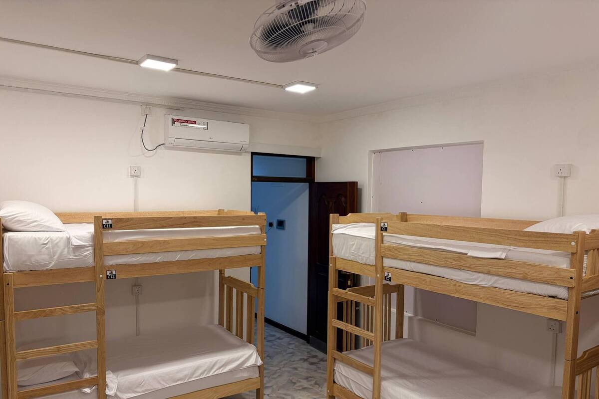 Due letti a castello in una stanza con ventilatore a soffitto, condizionatore d'aria e una porta.