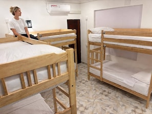 Bunk beds in a room with a tiled floor, a white air conditioner, and a door. - Hostel City Centre by Janatha (Colombo)