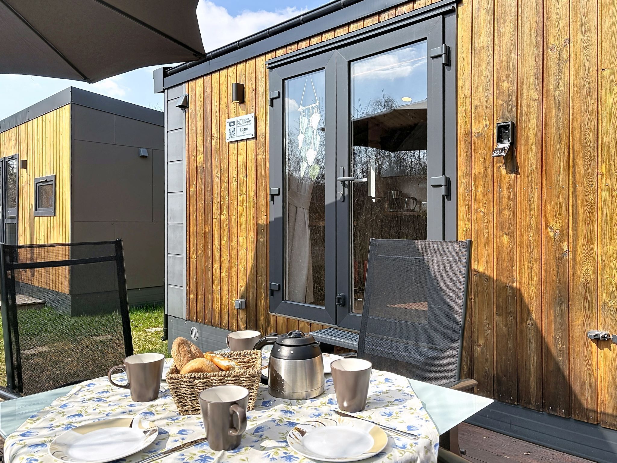 A wooden exterior wall with a sliding glass door, a sign, and a table set with breakfast items.