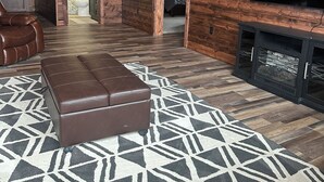 A log cabin interior with a leather sofa, a patterned rug, a television, and a fireplace.