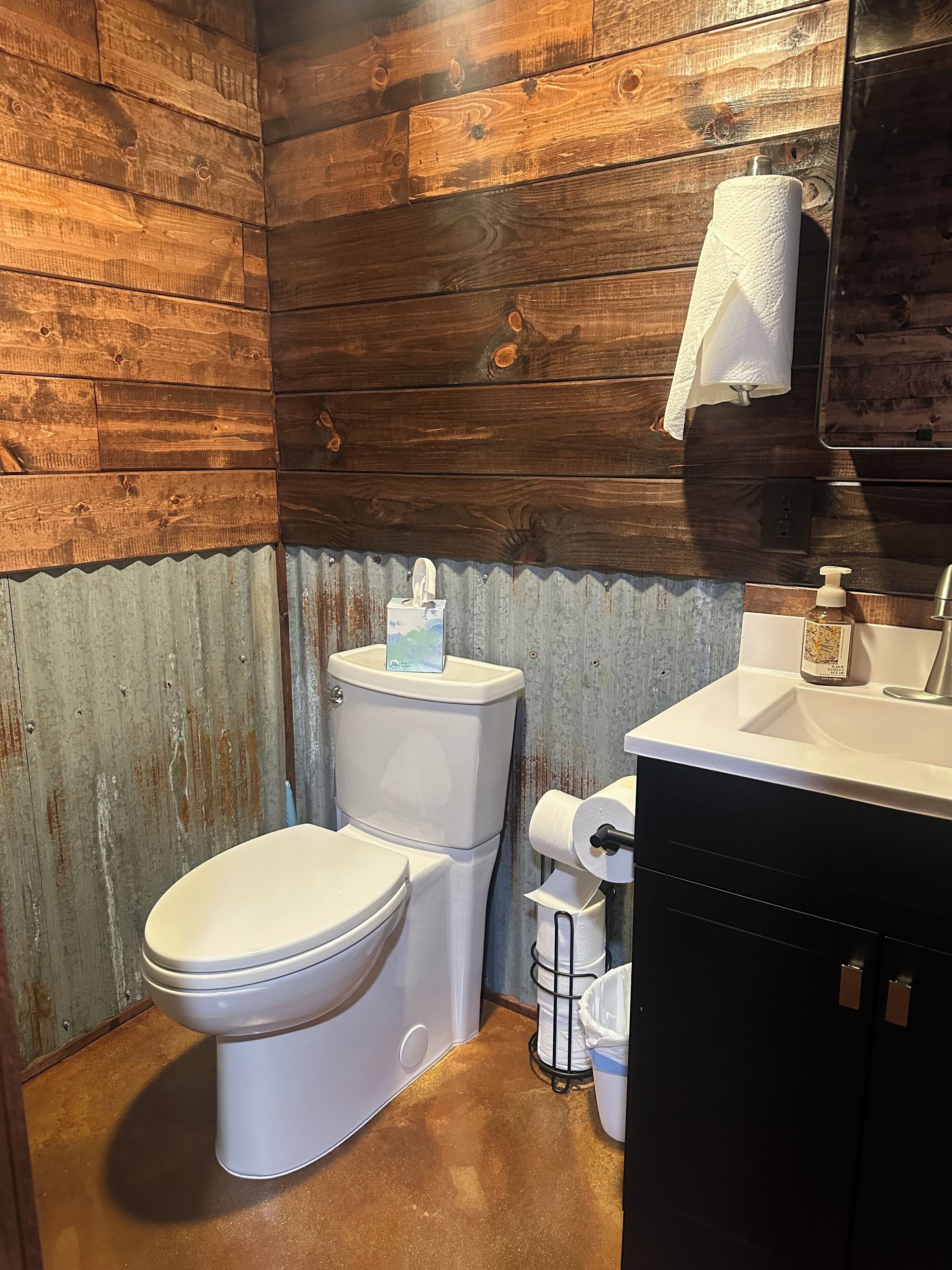 Une salle de bain avec un mur en bois, des toilettes, un lavabo et un sèche-mains.