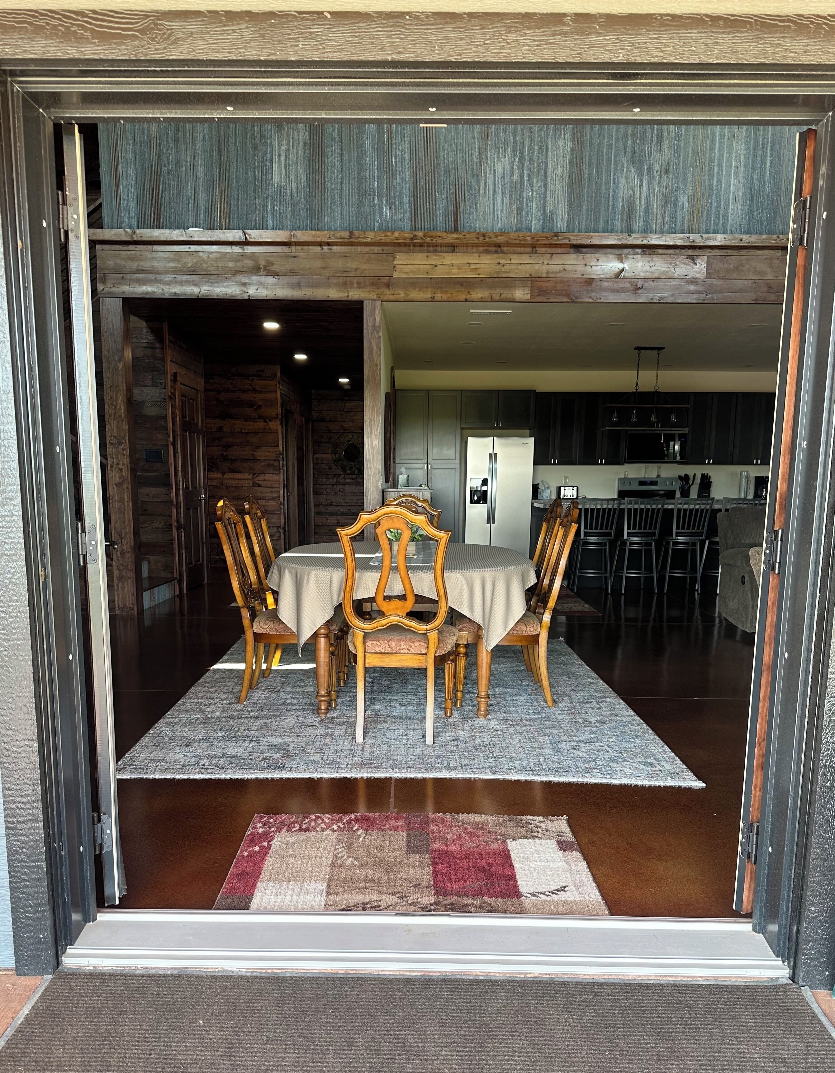 A dining area with a table and chairs, a kitchen in the background, and a wooden floor.