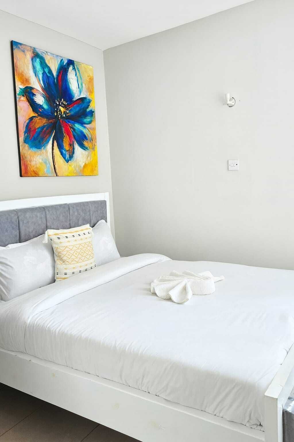 Un dormitorio con cama, almohada, manta, un cuadro y un interruptor de luz.