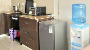 Cozinha compacta equipada com micro-ondas, torradeira e frigorífico, dispensador de água e uma pia pequena.