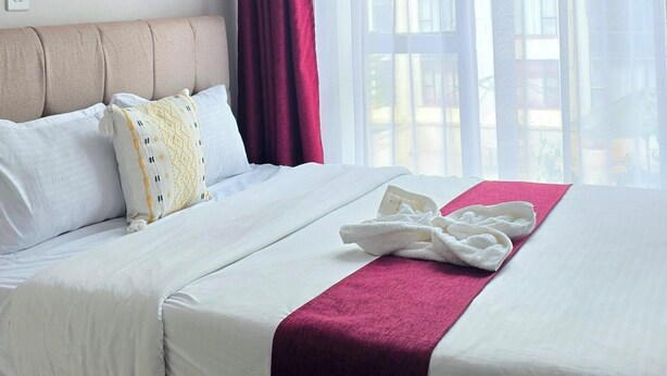 Quarto de hotel com cama, janela com cortinas e vista para edifícios.