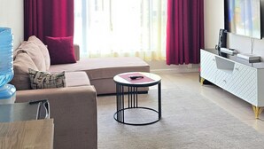 Uma sala de estar com sofá, mesa de centro, televisão e janela com cortinas.