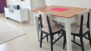 Uma área de refeições com uma mesa e cadeiras de madeira, um armário branco com uma televisão e uma porta que dá para outro cômodo.