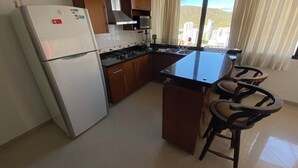 Een keuken met een koelkast, fornuis, magnetron, en een eethoek met stoelen.
