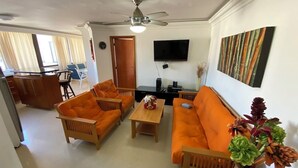 Een woonkamer met oranje meubels, een plafondventilator, een flatscreen-tv en een kunstwerk aan de muur.