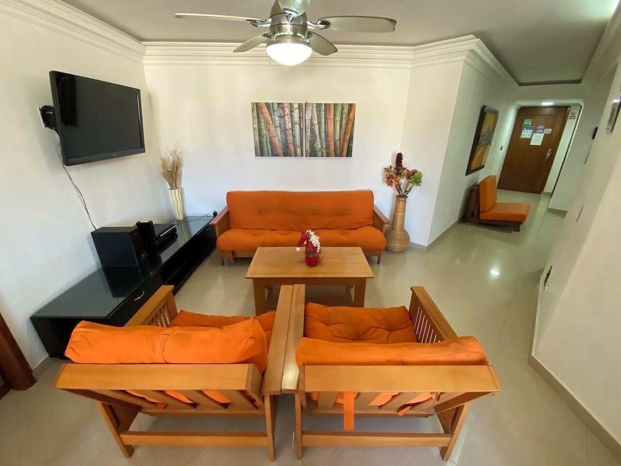 A living room with a sofa, two armchairs, a coffee table, a TV, and a ceiling fan.