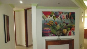Een hal met een kleurrijke muurschildering van een luchtballon, een ingelijste foto aan de linkerkant en een houten consoleschrank met een vaas.