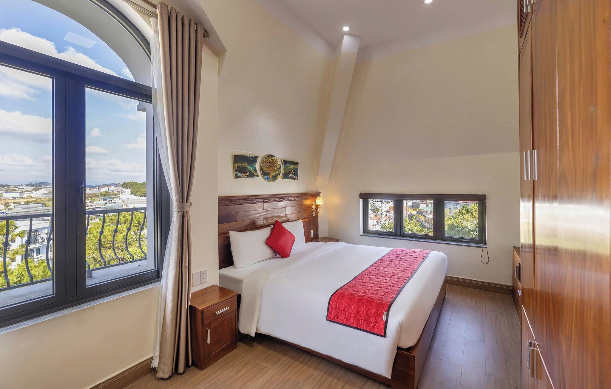 A bedroom with a large window, a bed with a red throw, and a view of the cityscape.