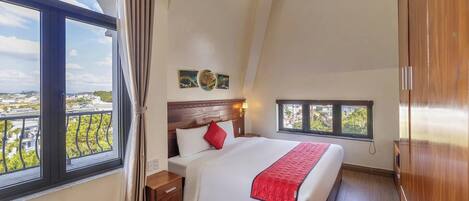 A bedroom with a large window, a bed with a red throw, and a view of the cityscape.