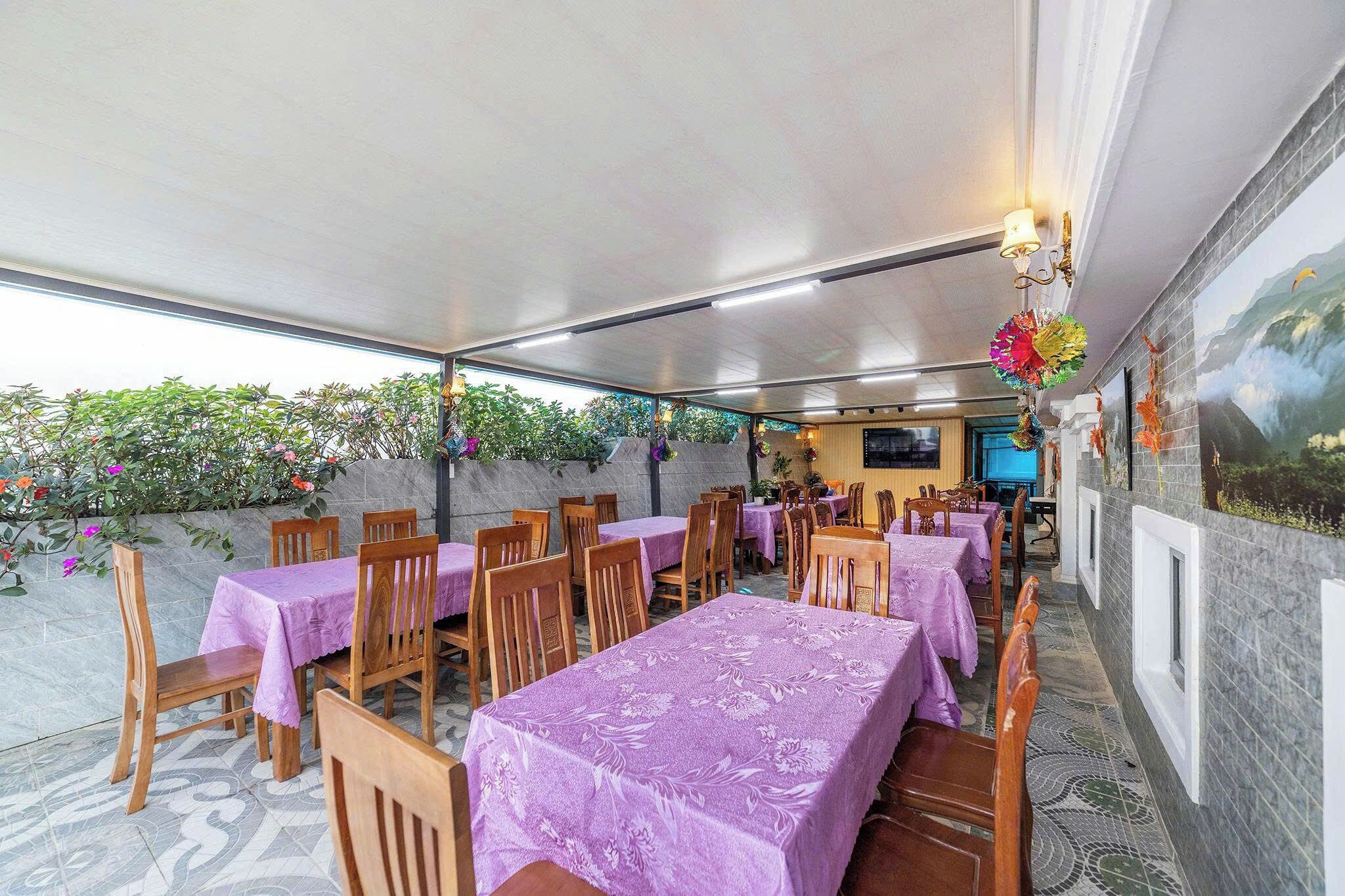 An indoor dining area with tables covered in purple tablecloths, wooden chairs, and a tiled floor.