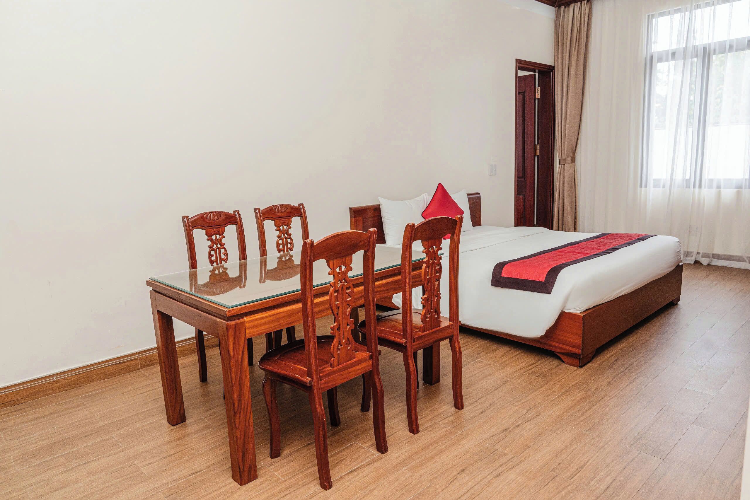 A hotel room with a bed, a wooden dining table with chairs, and a window with curtains.