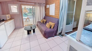 A cozy room with a sofa, a small table, a kitchen area, and a sliding glass door leading to an outdoor area. - Villa Ecureuils by Interhome (Mimizan)