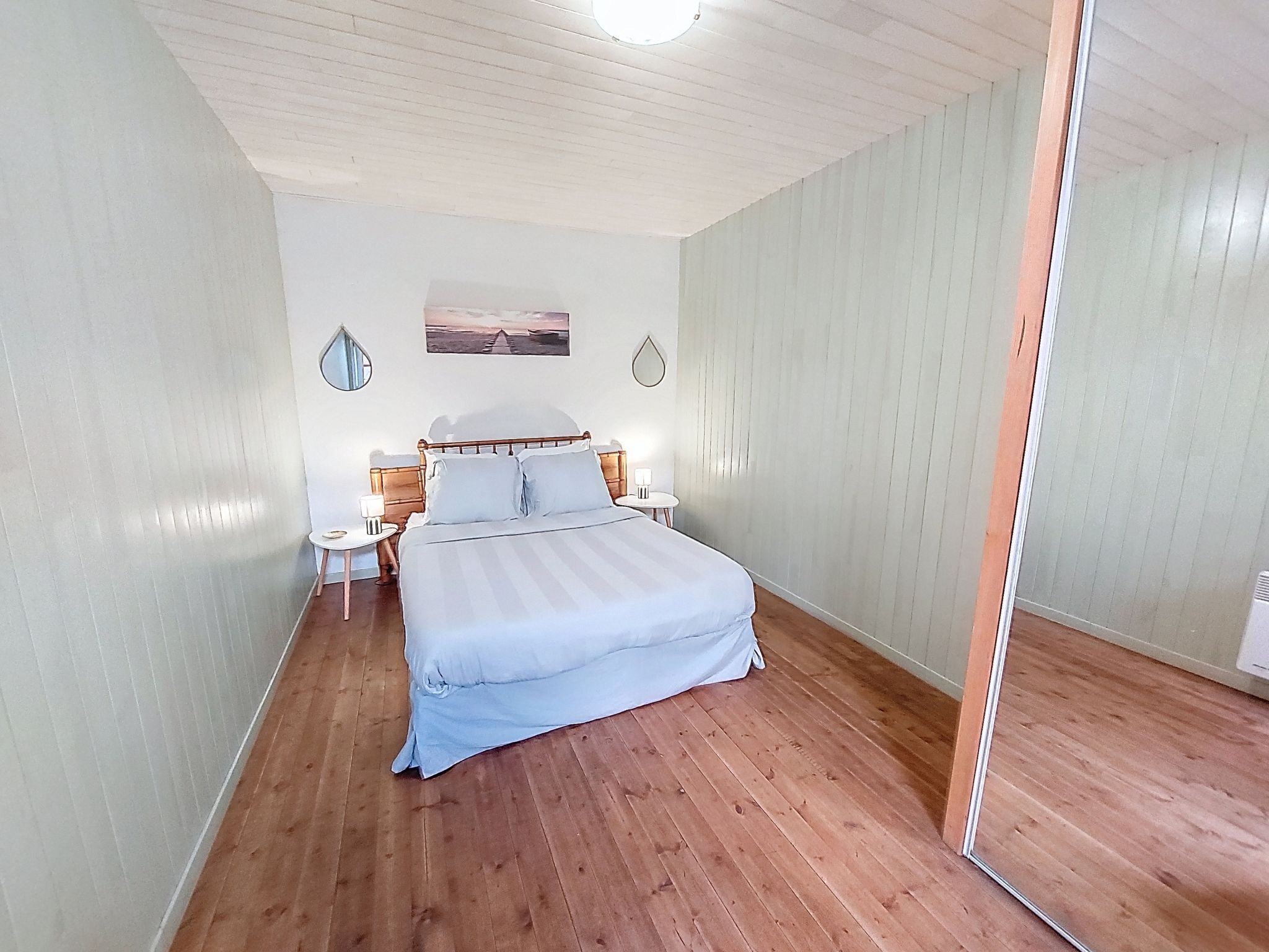 Een slaapkamer met een bed, nachtkastjes, een spiegel en een aan de muur hangend schilderij.