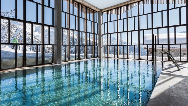 An indoor swimming pool with large windows offering views of snow-covered mountains.