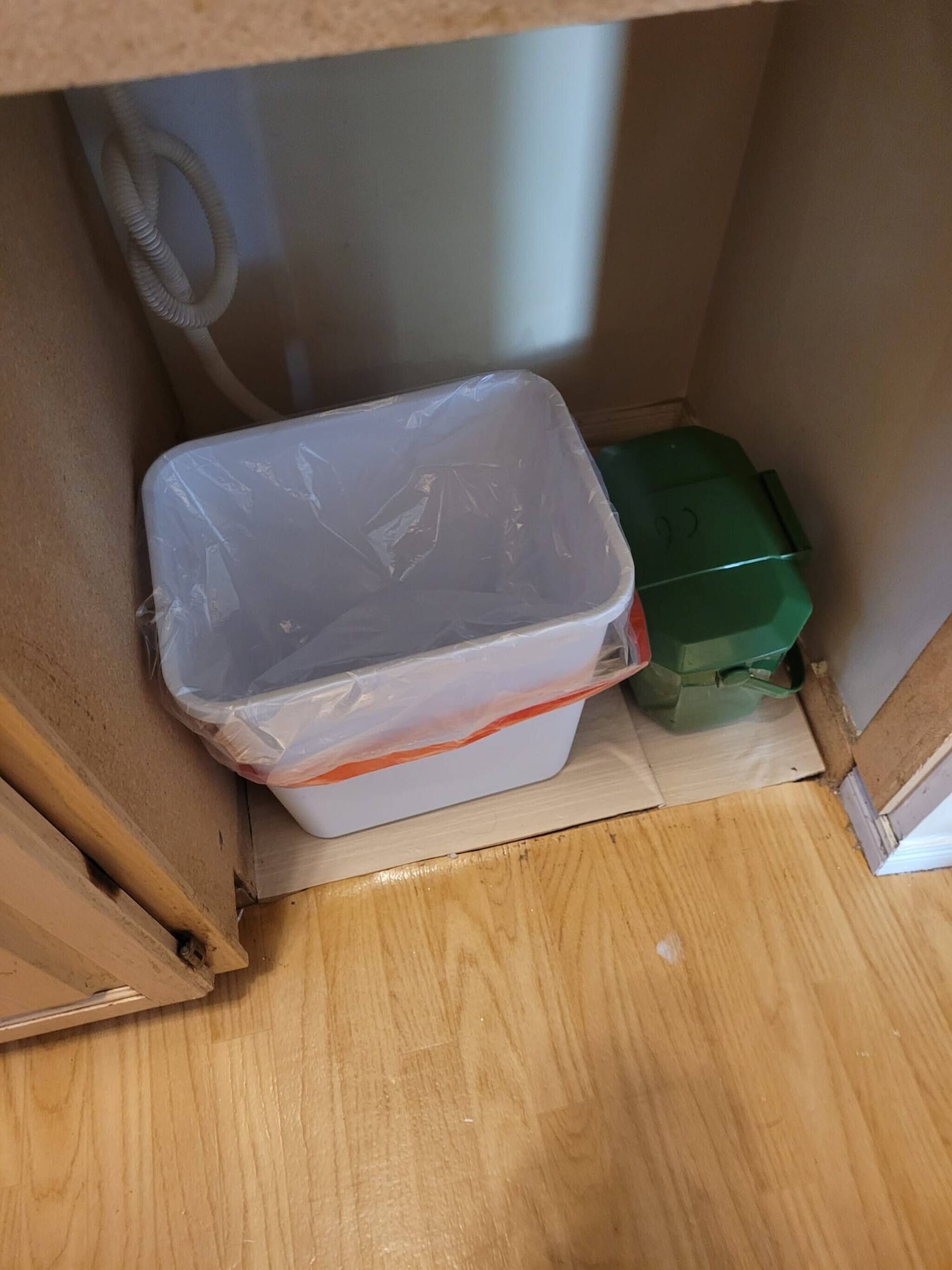 Un recipiente de plástico con una correa roja, un objeto verde y un suelo de madera.