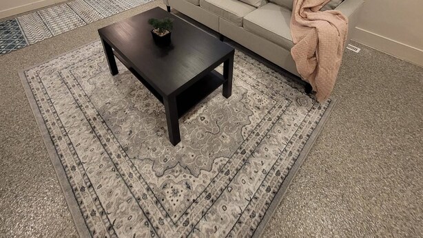 Ein Wohnzimmer mit einer Couch, einem Couchtisch, einem gemusterten Teppich und einem Essbereich mit Stühlen.