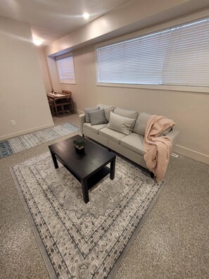 Un salon comprenant un canapé, une table basse, un tapis à motifs et un coin repas avec des chaises.