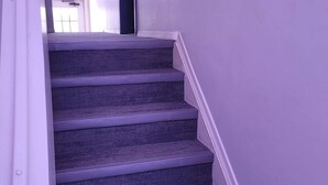 Eine Treppe mit einem strukturierten Teppich, weißen Wänden und einer Tür am oberen Ende.