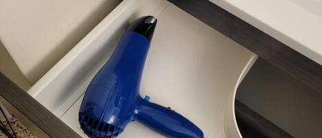A blue hair dryer in a drawer with a white countertop and a black cable.