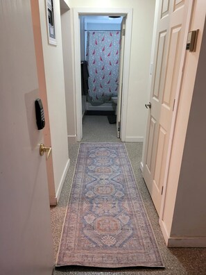 Ein Flur mit einem gemusterten Teppich, einer Tür mit Schloss und einem Badezimmer mit Duschvorhang.