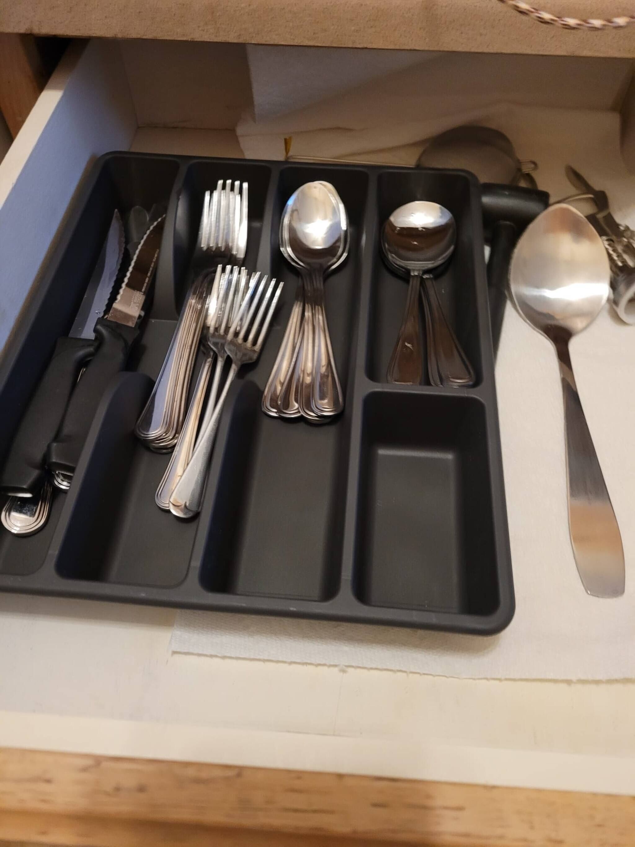 A black tray with cutlery including forks, spoons, and a knife, and a small rectangular compartment.