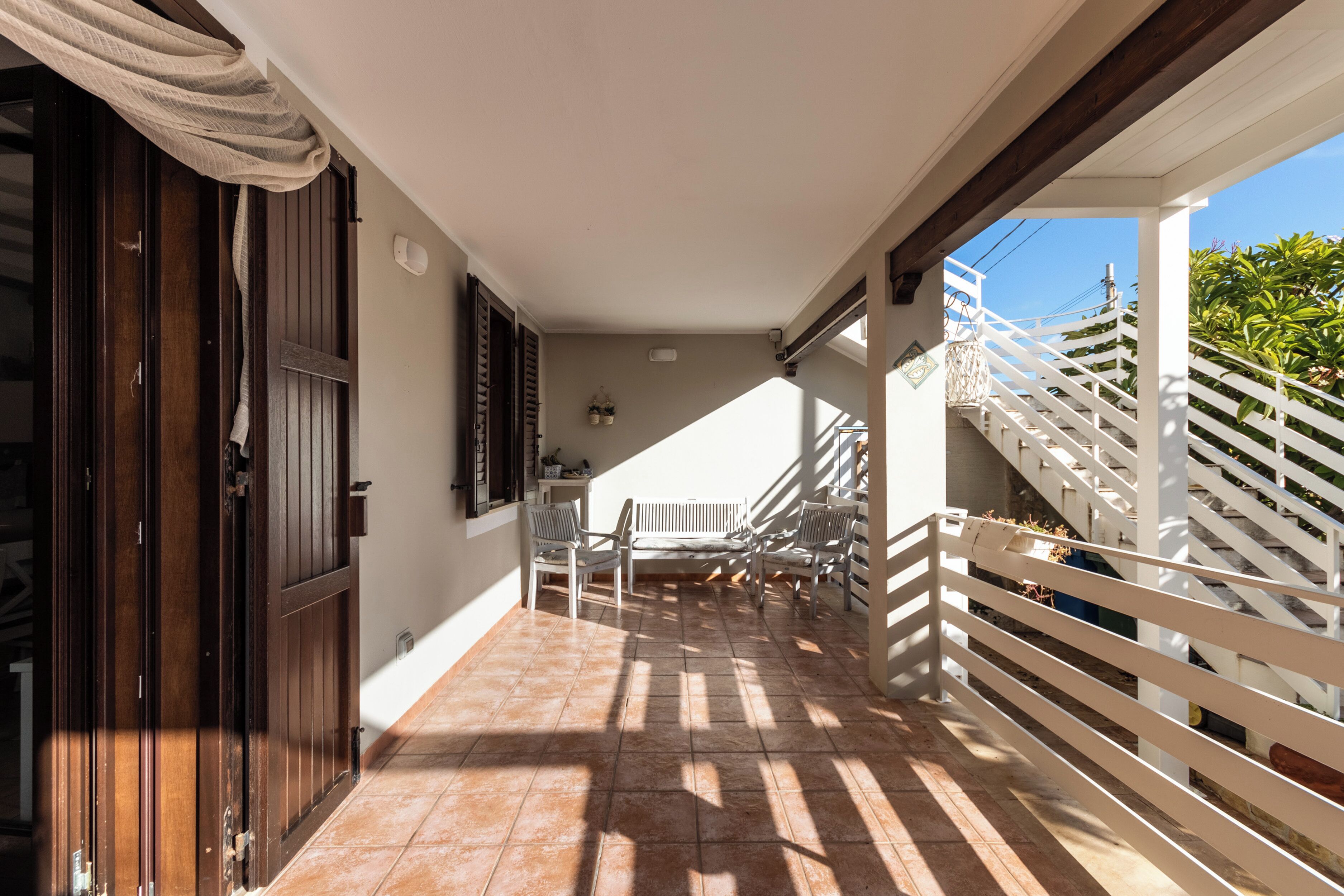 A covered balcony with a tiled floor, a wooden door, and a white railing.
