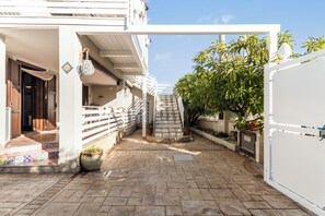 A courtyard with a staircase leading to a balcony, potted plants, and a white wall. - Two Steps from the Sea Down (Gallina)