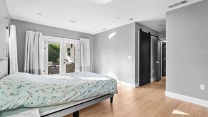 A bedroom with a bed, a window with curtains, a door, and a hallway leading to another room. - 3BR Retreat w/ Pool & Spa, Prime Tarzana Location (Los Angeles)