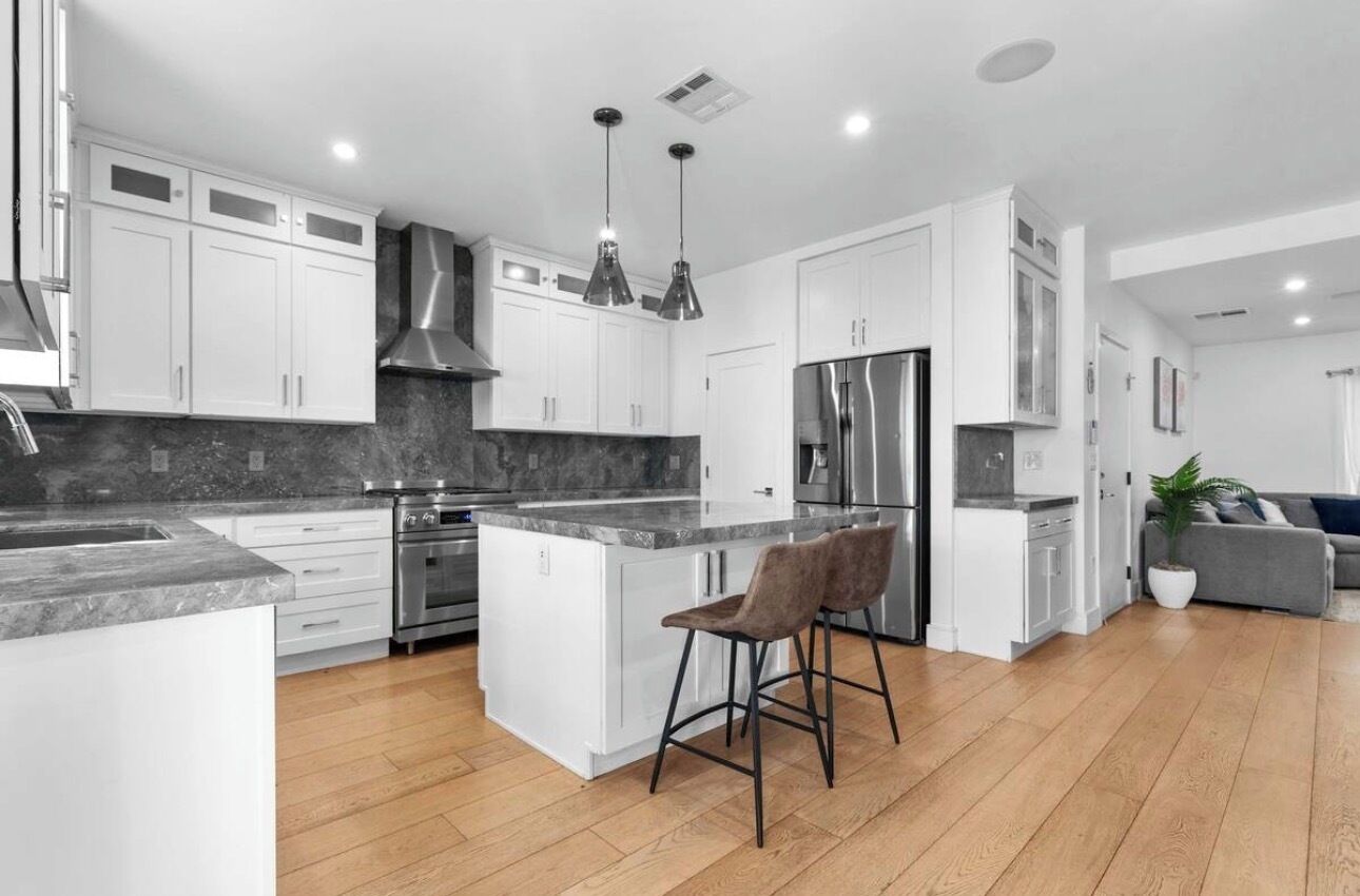 A modern kitchen with white cabinetry, stainless steel appliances, and a central island with bar stools.