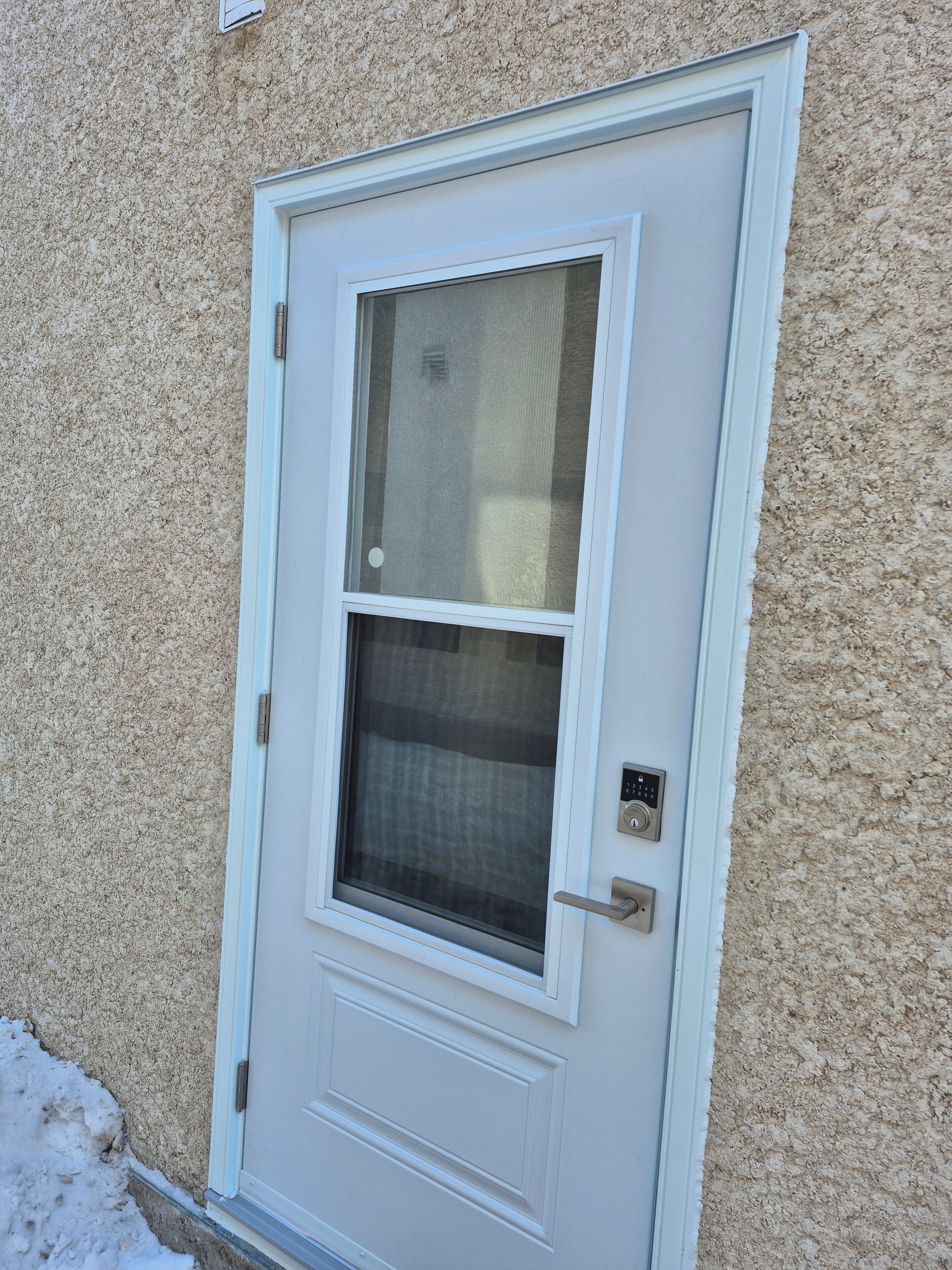 A white door with a window, a keypad lock, and a small outdoor area with snow.