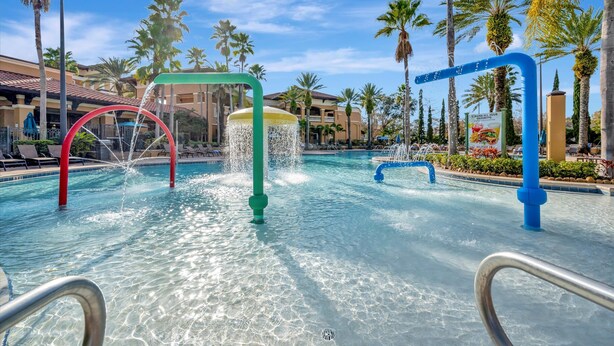 Une piscine dotée de plusieurs éléments aquatiques, entourée de palmiers et d’immeubles d’hôtel.