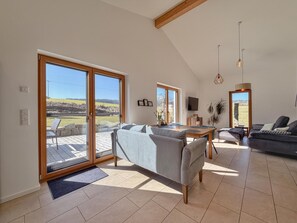 A spacious living area with a large sliding glass door leading to an outdoor patio, a dining table, and a comfortable seating arrangement. - Modern holiday home in Bavaria with garden (Neunburg v.W.)