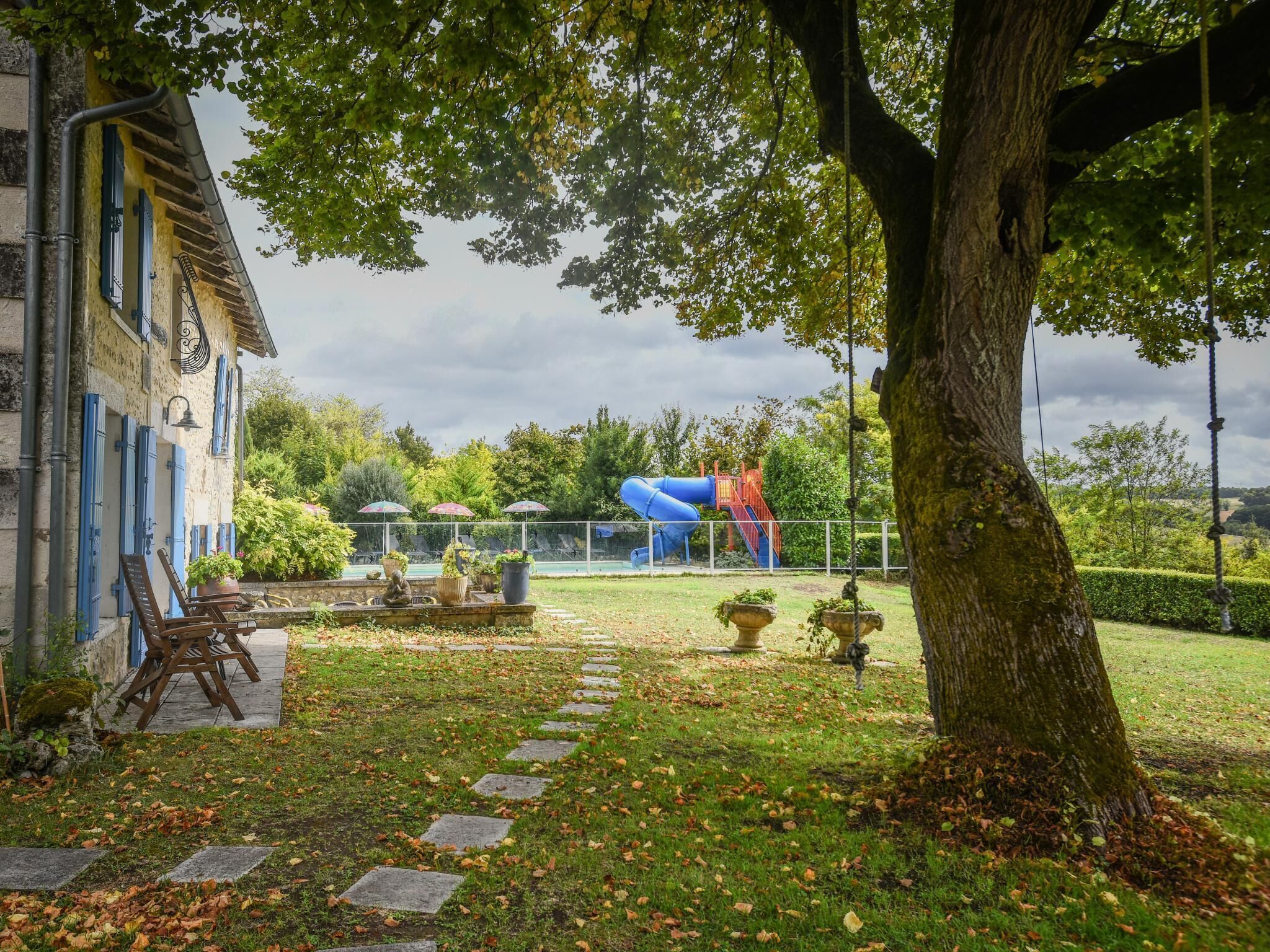 Ein Garten mit einem Kiesweg, einem Baum und einem Spielplatz mit einer Rutsche.