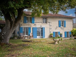 Ein zweistöckiges Steinhaus mit blauen Fensterläden, einer Schaukel und einem großen Baum im Garten.