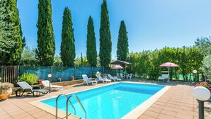 A rectangular swimming pool with a tiled deck, surrounded by lounge chairs and umbrellas, with tall trees in the background. - Preselle by Interhome (Casale Marittimo)